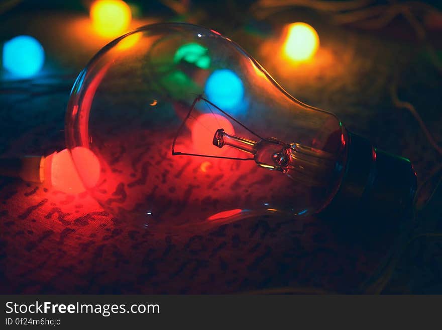 An incandescent light bulb with colorful lights in the background. An incandescent light bulb with colorful lights in the background.