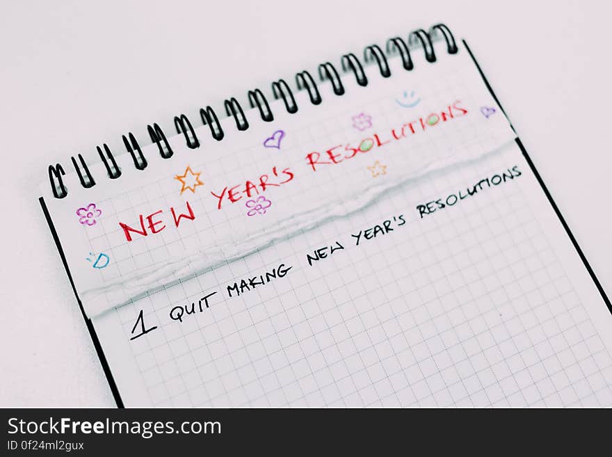 Spiral bound notebook with text at top of page in bold red uppercase letters "new years resolutions" and below it in black "1 quit making new year's resolutions".