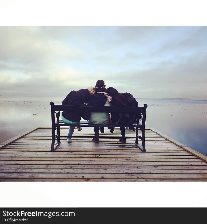 Three friends sitting on a bench at lakeside. Three friends sitting on a bench at lakeside.