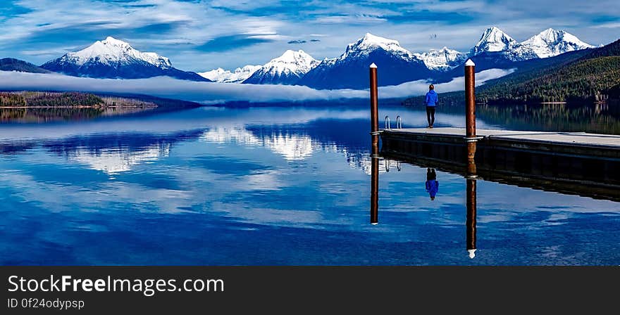 Rear view of person stood on Alpine lake pier with snow capped mountains range in background. Rear view of person stood on Alpine lake pier with snow capped mountains range in background.