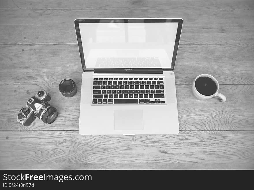 An open laptop, camera and a cup of coffee on a wooden background. An open laptop, camera and a cup of coffee on a wooden background.