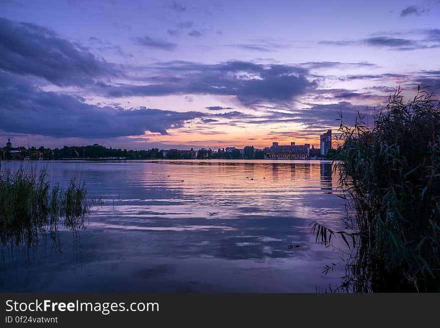 A lake at sunset with buildings on the shore.