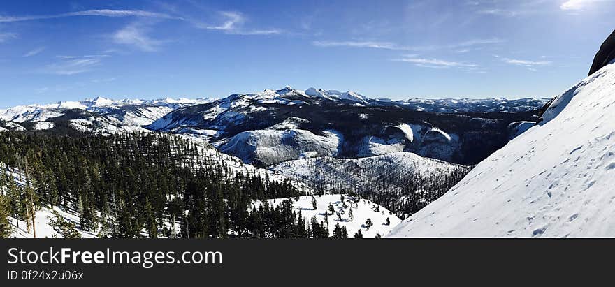 A landscape with snowy hills and forests with blue skies.