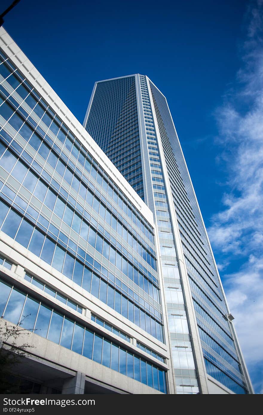 Modern architect designed skyscraper (tower block) built of concrete and glass with blue sky and thin cloud reflecting in the windows. Modern architect designed skyscraper (tower block) built of concrete and glass with blue sky and thin cloud reflecting in the windows.