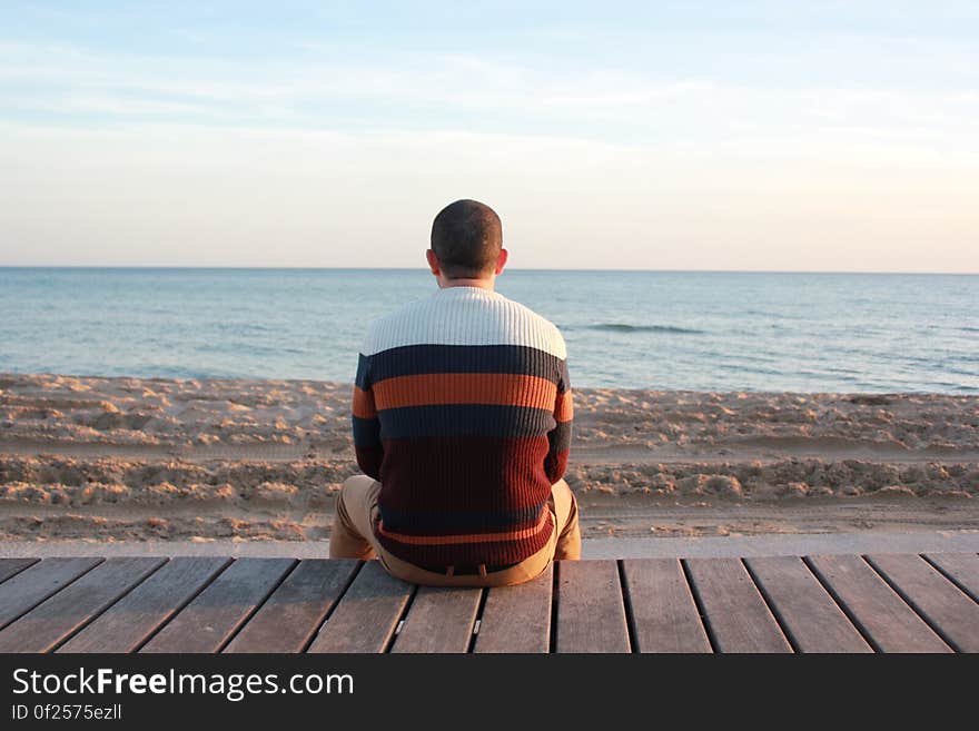 Man Sitting on Wooden Panel Facing in the Ocean