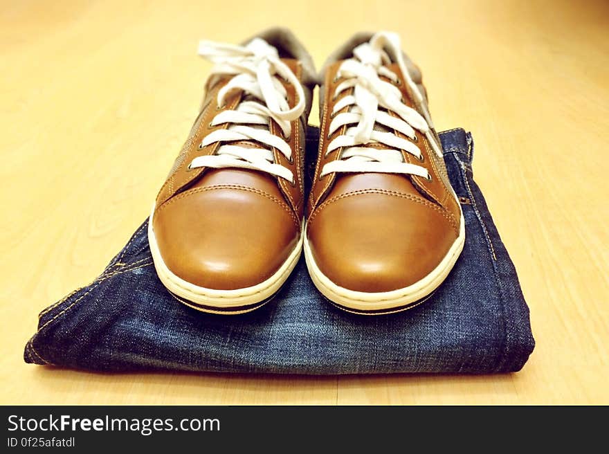 Men's brown leather shoes and jeans on a table.