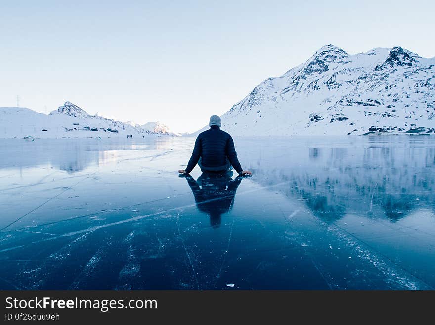 A man sitting on ice on a clear mountain lake. A man sitting on ice on a clear mountain lake.