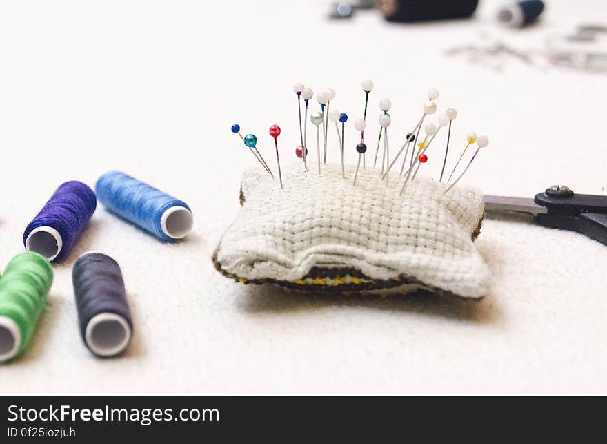 White Blue and Red Needle on White and Brown Pad Near Blue Green and Black Thread