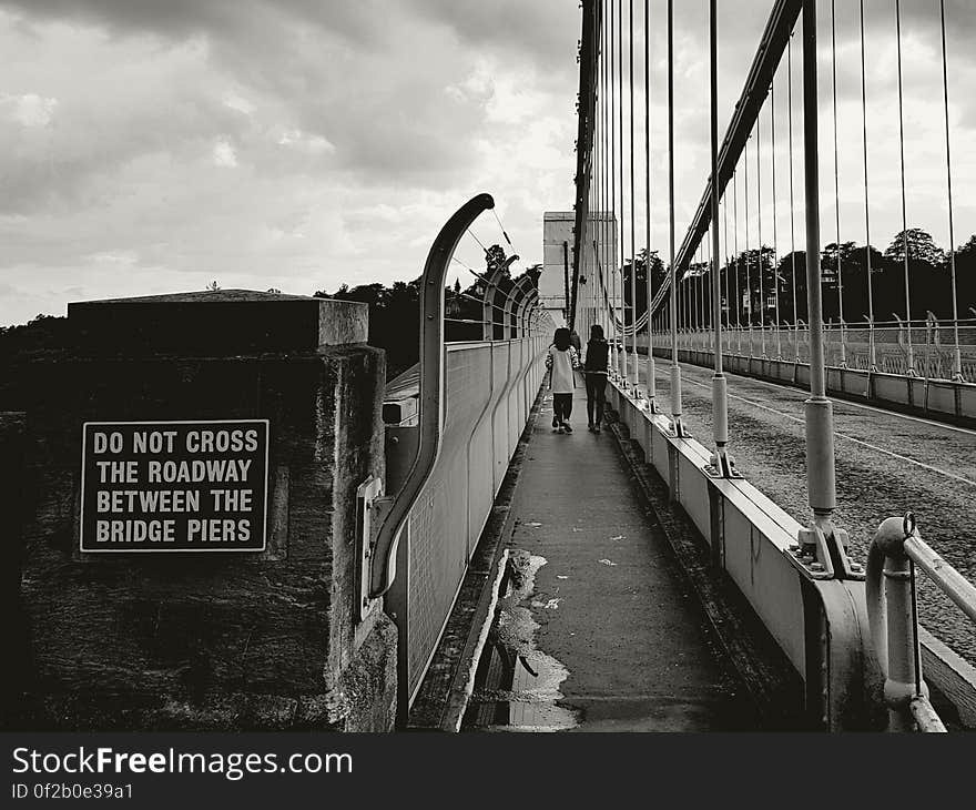 A black and white image of pedestrians crossing a bridge on a walkway next to the driveway. A black and white image of pedestrians crossing a bridge on a walkway next to the driveway.