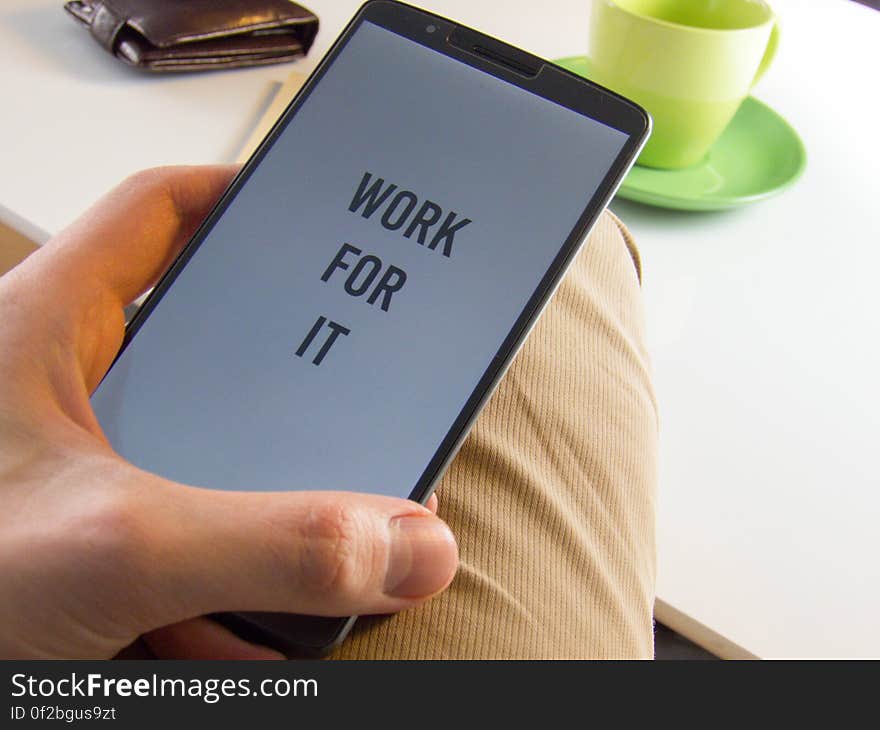 A close up of a man holding a smart phone with the text "work for it" on the screen.