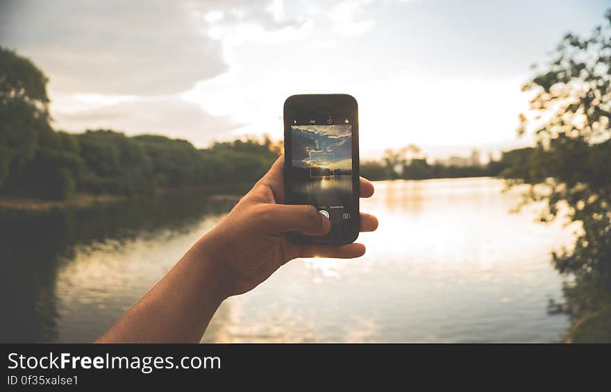 Close-up of Hand Holding Mobile Phone Against Lake