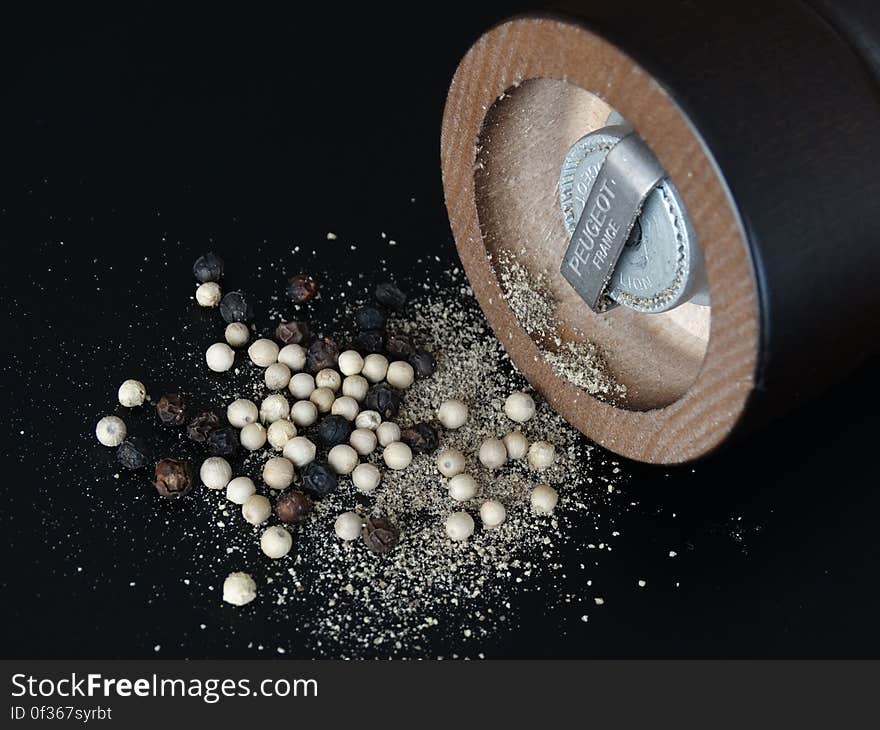 A close up of a pepper mill and whole and ground peppers. A close up of a pepper mill and whole and ground peppers.