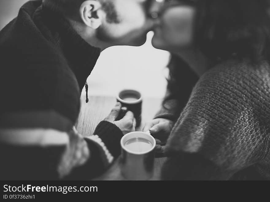 A black and white photo of a couple kissing holding coffee cups. A black and white photo of a couple kissing holding coffee cups.