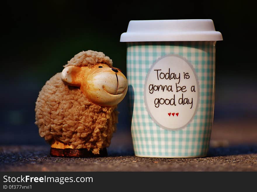 A take-away cup of coffee and a small sheep figure. A take-away cup of coffee and a small sheep figure.