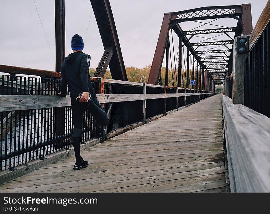 A man stretching his right leg on a wooden footbridge. A man stretching his right leg on a wooden footbridge.