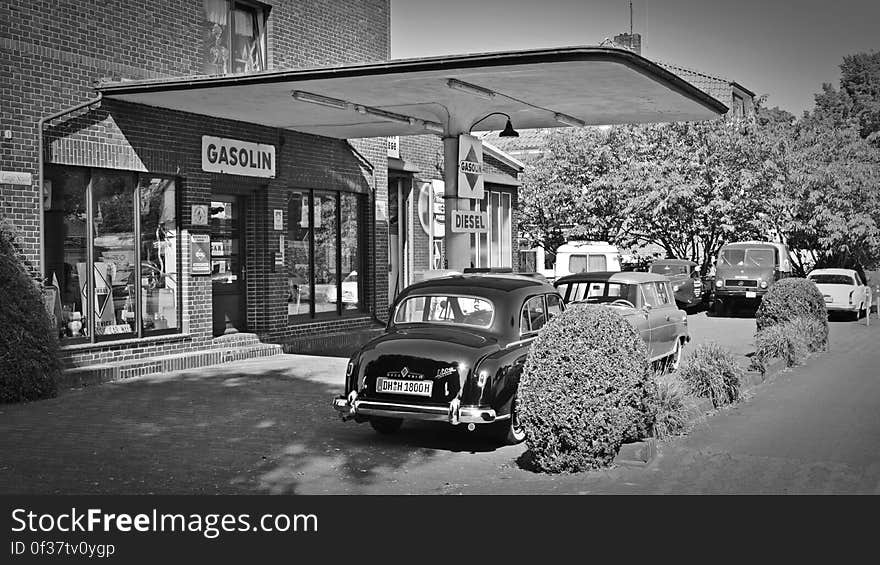 A black and white old fashioned gas station and vintage cars.