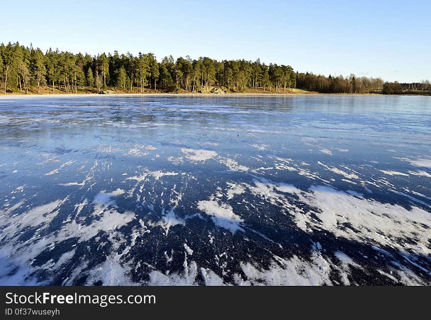 Swedish lake with white foam on blue waters and beyond it dense forest, pale blue sky. Swedish lake with white foam on blue waters and beyond it dense forest, pale blue sky.