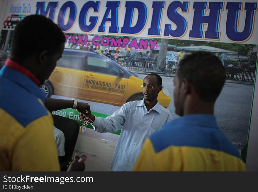 Suleiman Mohamed Daras &#x28;centre&#x29;, manager of the Mogadishu Taxi Company hands a set f keys to one of his drivers at the company&#x27;s head office in the Somali capital Mogadishu, 01 September 2013. Operating since the end of May of this year in the city&#x27;s dusty and once again bustling streets and thoroughfares, the MTC&#x27;s distinctive yellow and purple cars offer customers taxi fares around Mogadishu at competitive rates and in the first 3 months of operations, the company has increased it&#x27;s fleet of vehicles from an initial 25 to over 100. The company, according to one of it&#x27;s drivers, also enables employment opportunities for Somalia&#x27;s youth following two decades of conflict in the Horn of Africa nation that shattered a generation. Now, thanks to the relative peace that has followed the departure of the Al-Qaeda-affiliated extremist group Al Shabaab from the city; an internationally recognised government for the first time in years and thousands of Diaspora Somalis returning home to invest in and rebuild their country, the MTC is one of many new companies establishing itself in the new Mogadishu and offering services that were hitherto impossible to provide. AU-UN IST PHOTO / STUART PRICE. Suleiman Mohamed Daras &#x28;centre&#x29;, manager of the Mogadishu Taxi Company hands a set f keys to one of his drivers at the company&#x27;s head office in the Somali capital Mogadishu, 01 September 2013. Operating since the end of May of this year in the city&#x27;s dusty and once again bustling streets and thoroughfares, the MTC&#x27;s distinctive yellow and purple cars offer customers taxi fares around Mogadishu at competitive rates and in the first 3 months of operations, the company has increased it&#x27;s fleet of vehicles from an initial 25 to over 100. The company, according to one of it&#x27;s drivers, also enables employment opportunities for Somalia&#x27;s youth following two decades of conflict in the Horn of Africa nation that shattered a generation. Now, thanks to the relative peace that has followed the departure of the Al-Qaeda-affiliated extremist group Al Shabaab from the city; an internationally recognised government for the first time in years and thousands of Diaspora Somalis returning home to invest in and rebuild their country, the MTC is one of many new companies establishing itself in the new Mogadishu and offering services that were hitherto impossible to provide. AU-UN IST PHOTO / STUART PRICE.