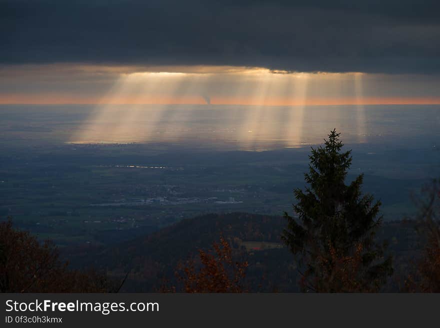 Sun beams over landscape from behind clouds at sunrise.