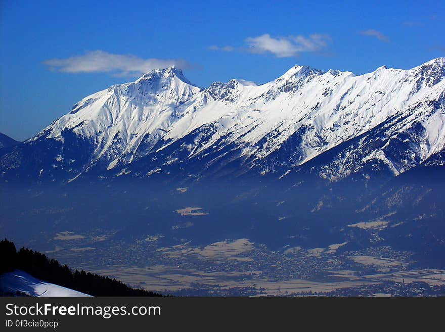 Landscape of snow capped mountain peaks and valley against blue skies on sunny day.