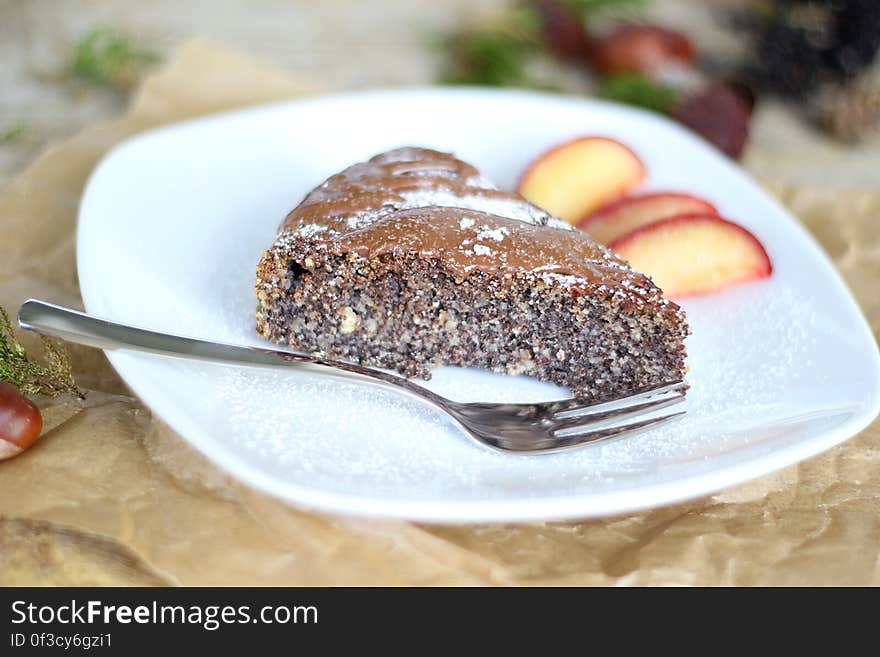 Piece of a baked chocolate dessert with fruit garnish and silver fork to the side on a white dish.