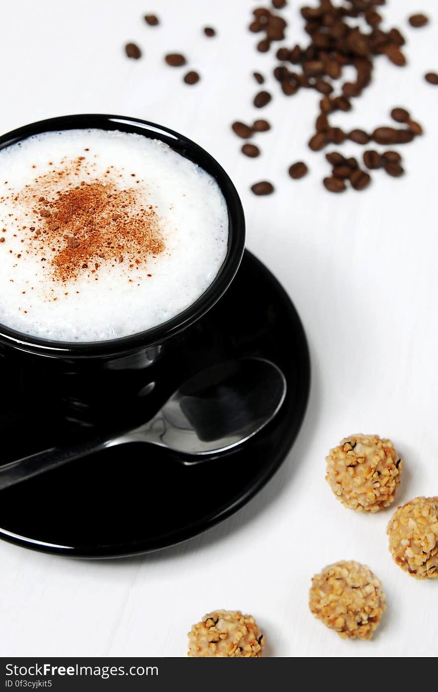 A close up of a cup of cappuccino with cinnamon on top, coffee beans and cookies beside.