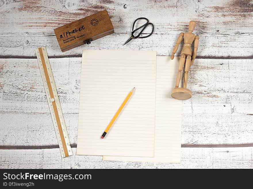 Blank page of paper with yellow pencil, ruler, scissors and wooden figurine on worn wooden slats. Blank page of paper with yellow pencil, ruler, scissors and wooden figurine on worn wooden slats.