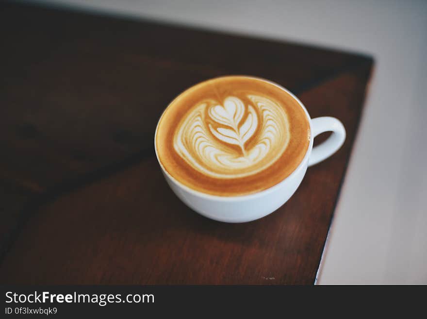 White china cup of cappuccino with design in froth on wooden table. White china cup of cappuccino with design in froth on wooden table.