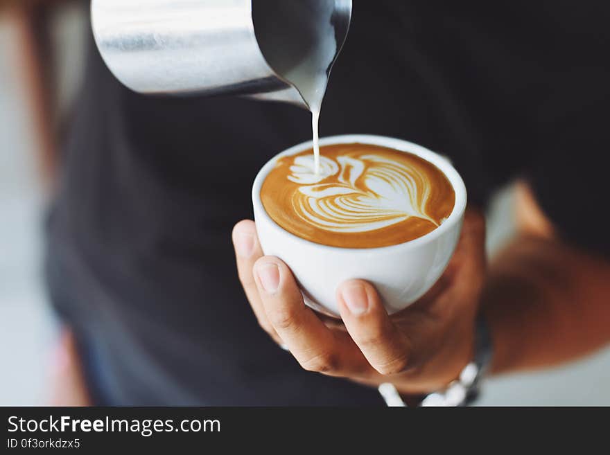 A barista pouring milk foam into a cup making latte art. A barista pouring milk foam into a cup making latte art.