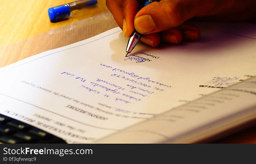 A close up of a hand signing a formal document with a pen. A close up of a hand signing a formal document with a pen.