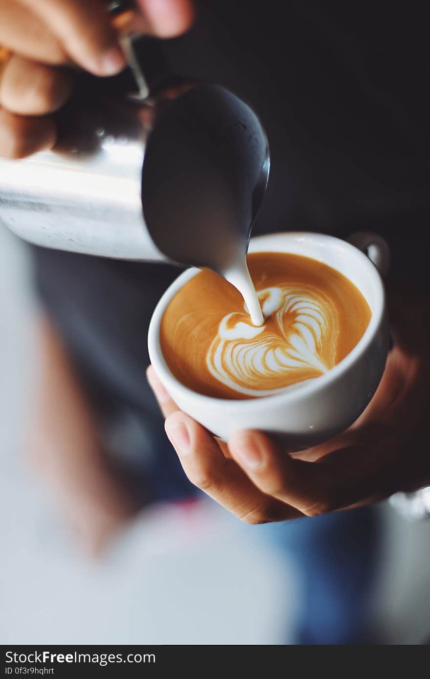 A close up of a hand adding milk to a cup of cappuccino. A close up of a hand adding milk to a cup of cappuccino.