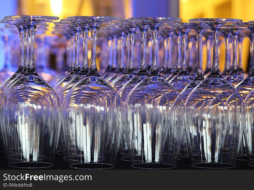 Rows of upturned wine glasses in a bar with colorful light reflection. Rows of upturned wine glasses in a bar with colorful light reflection.