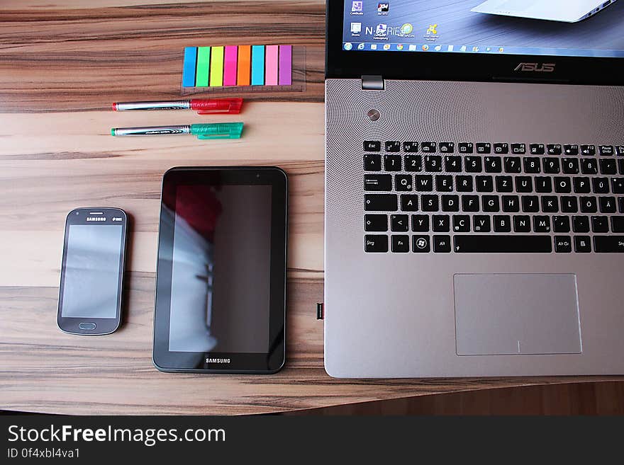 A laptop computer next to a tablet and a mobile phone on a desk. A laptop computer next to a tablet and a mobile phone on a desk.