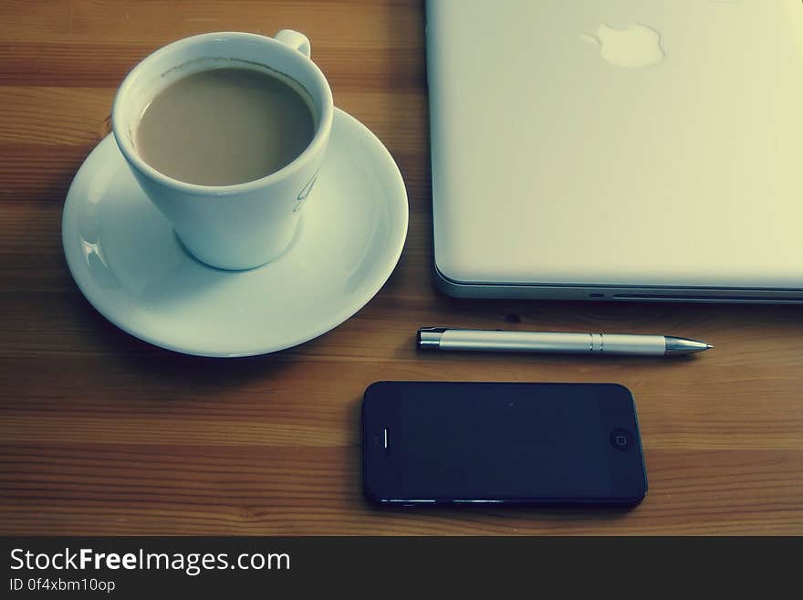 A laptop computer next to a cup of coffee, a smartphone and a pen. A laptop computer next to a cup of coffee, a smartphone and a pen.