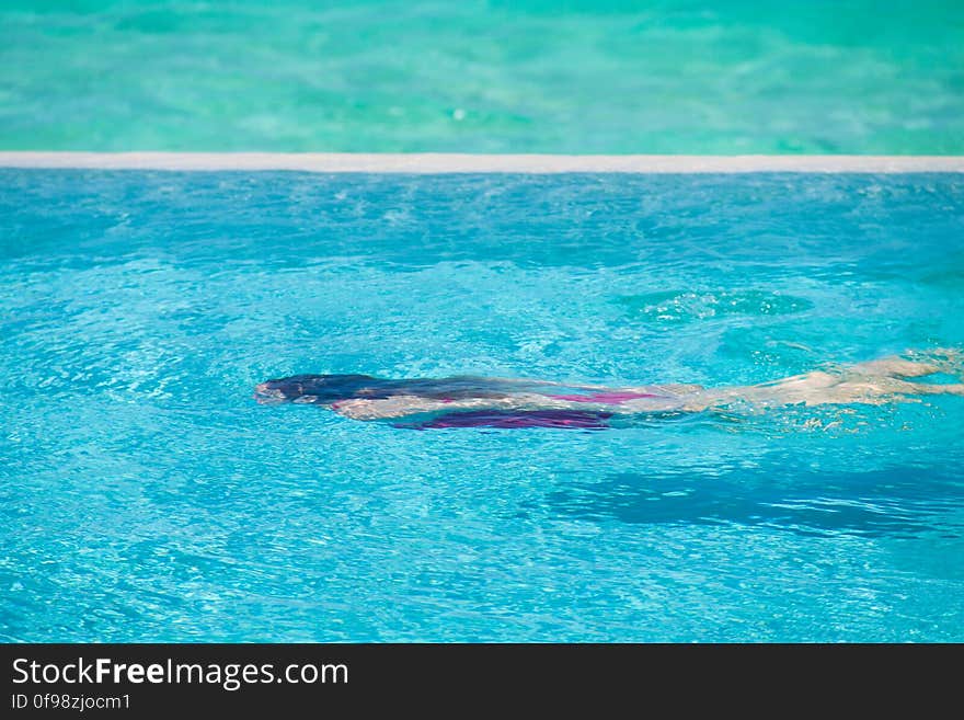 Girl in red swimming suit swimming underwater in a blue pool. Girl in red swimming suit swimming underwater in a blue pool