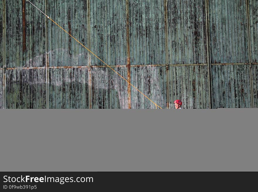 Man on wake board against exterior corrugated metal wall.