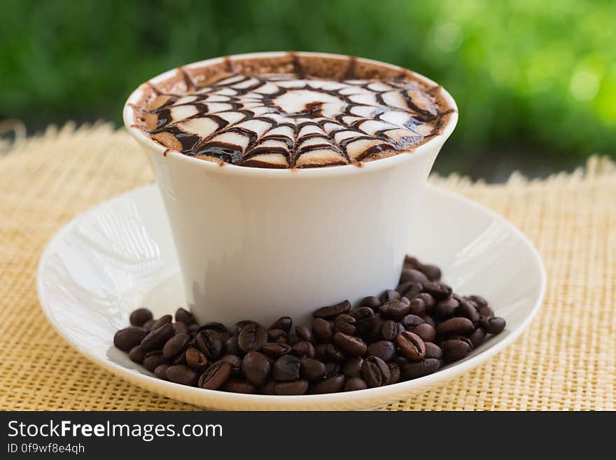 Decorative pattern on cup of coffee outdoors with beans, hessian sack background. Decorative pattern on cup of coffee outdoors with beans, hessian sack background.