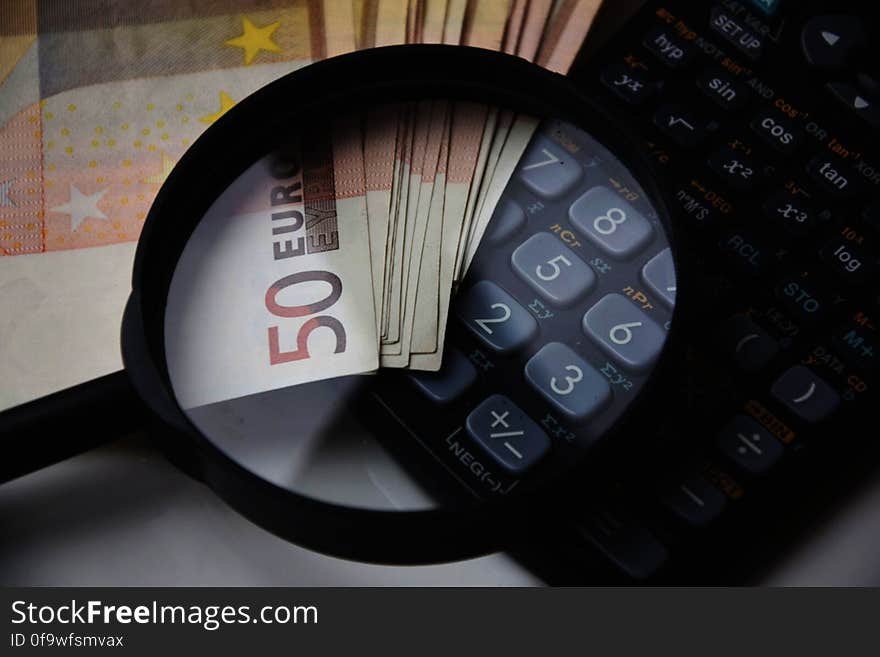 Close up of fifty Euro note denomination bills under magnifying glass with calculator. Close up of fifty Euro note denomination bills under magnifying glass with calculator.