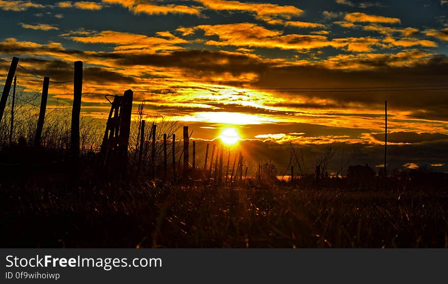 Sunset over country field with silhouette of wooden fence.