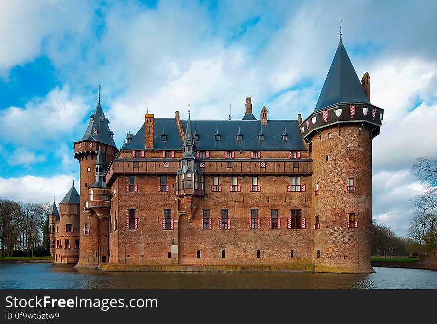 Facade of brick medieval castle surrounded by moat against blue skies with clouds. Facade of brick medieval castle surrounded by moat against blue skies with clouds.