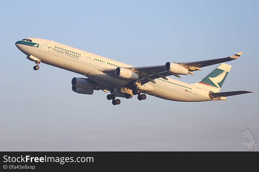 Cathay Pacific plane with cream and blue colors and four jet engines coming in to land, wheels down after a long haul flight, pale blue sky. Cathay Pacific plane with cream and blue colors and four jet engines coming in to land, wheels down after a long haul flight, pale blue sky.