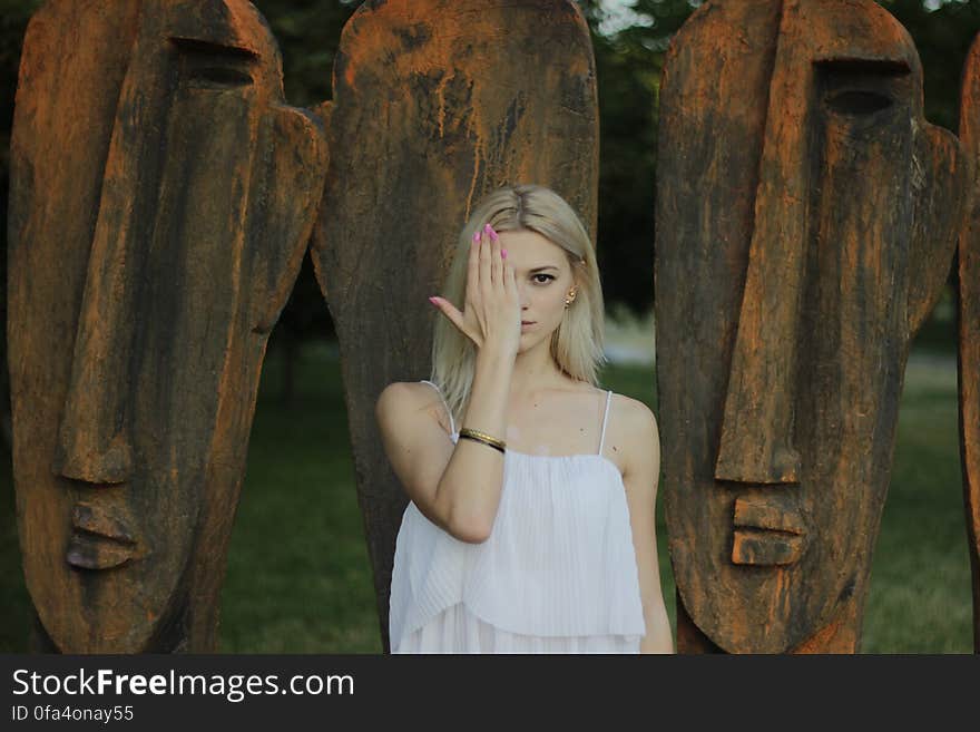 Woman Covering Face With Right Hand in Front of Large Tribal Head Statue