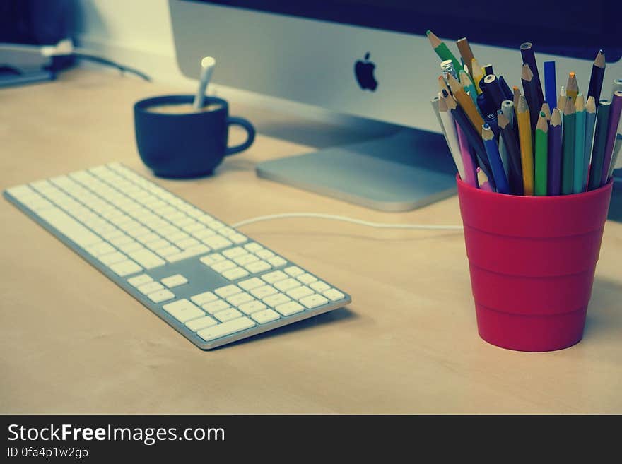 Blue Green and Black Colored Pencils on Red Plastic Cup Beside Silver Imac