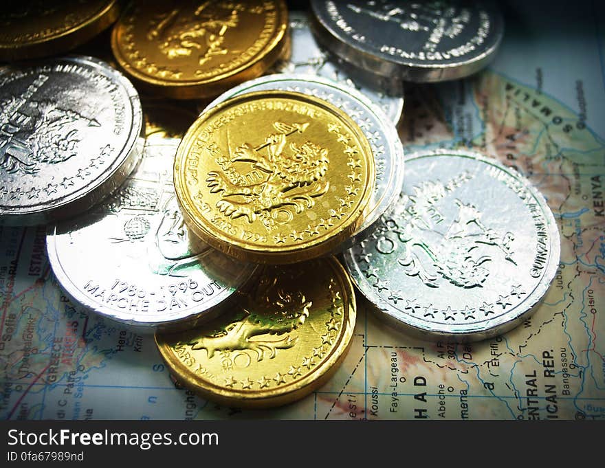 Different currency gold and silver coins on world map of continents of Europe and Africa.