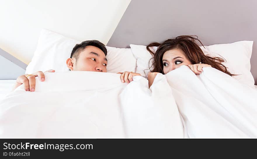 Young Asian couple hiding under white sheets and bedspread in home bedroom. Young Asian couple hiding under white sheets and bedspread in home bedroom.