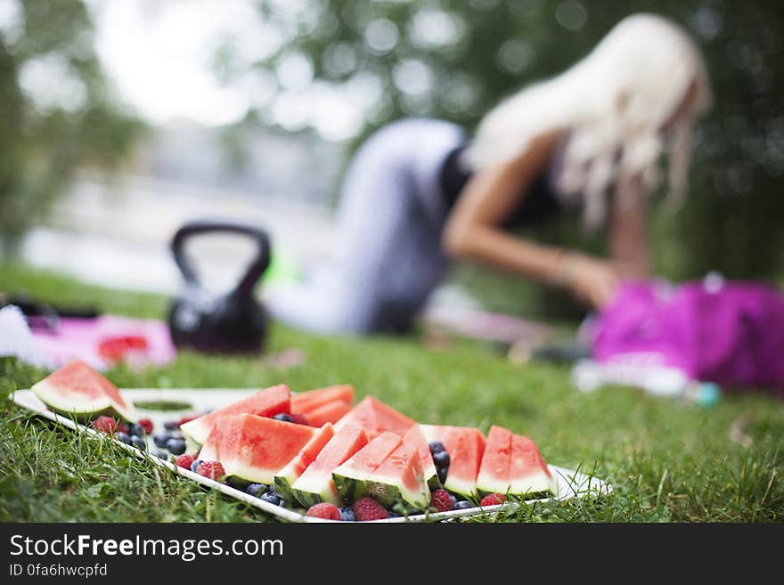 Fresh watermelon slices on tray on grass with blur of woman outdoors on picnic. Fresh watermelon slices on tray on grass with blur of woman outdoors on picnic.