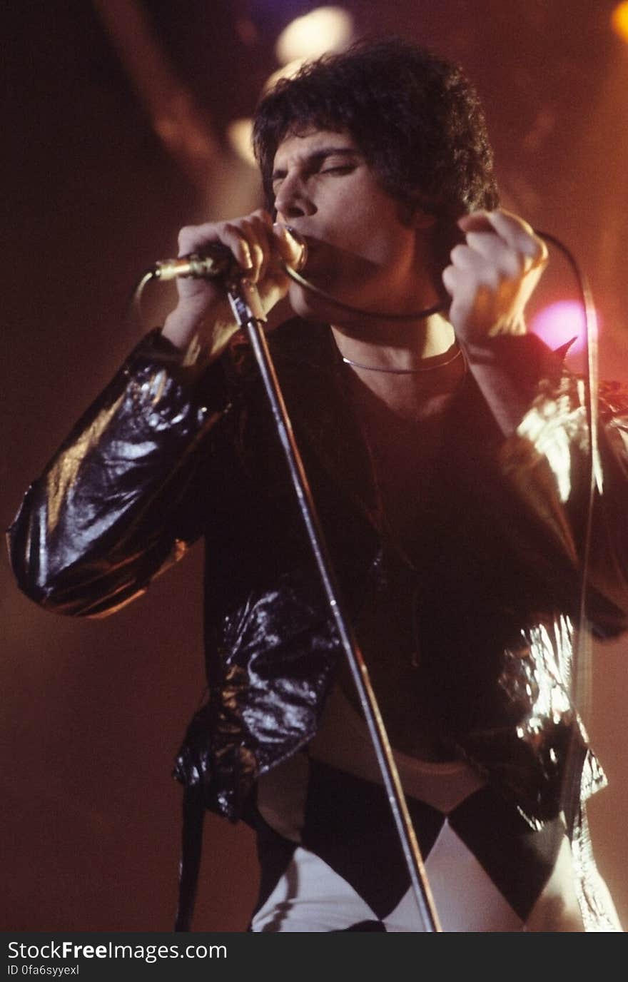 Freddie Mercury singing into microphone on-stage. Freddie Mercury singing into microphone on-stage.