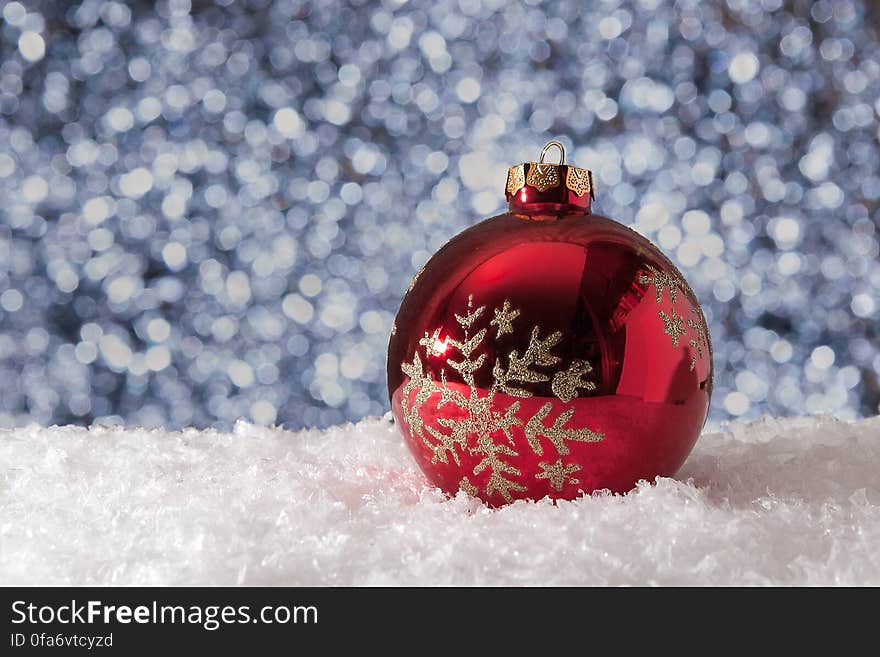 A close up of a red Christmas ball in the snow and blurred snowflakes in the background. A close up of a red Christmas ball in the snow and blurred snowflakes in the background.