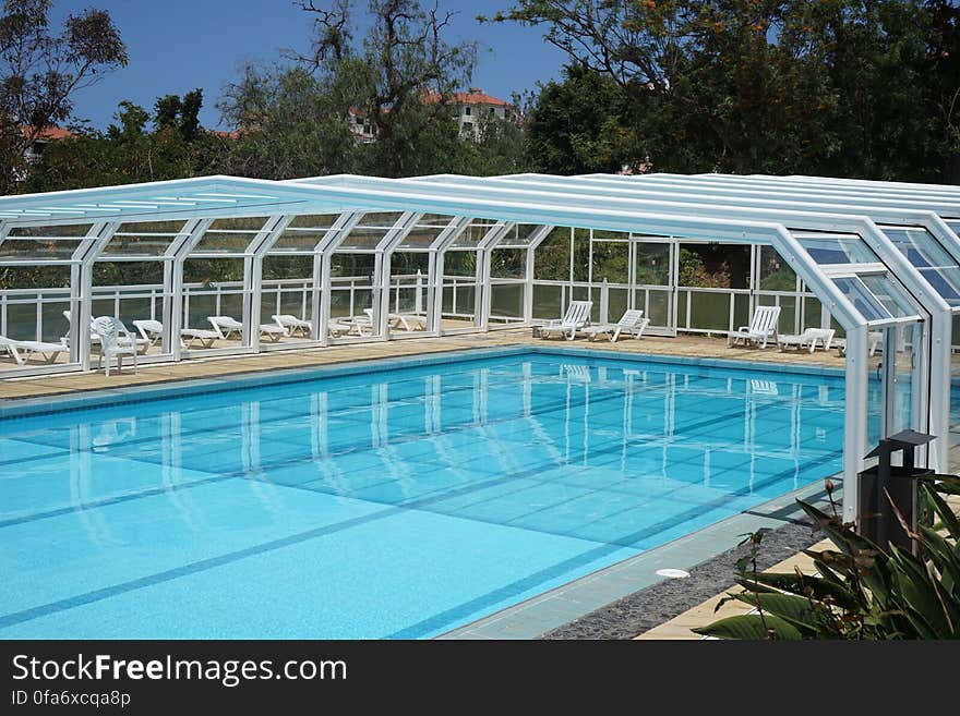 An empty partly covered outdoor swimming pool and sunbeds around. An empty partly covered outdoor swimming pool and sunbeds around.