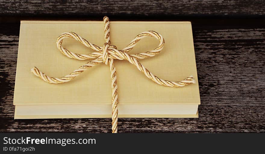 Blank hard cover book tied in gold ribbon on rustic wooden table. Blank hard cover book tied in gold ribbon on rustic wooden table.